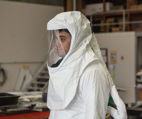 A man wearing respiratory protective equipment and protective gear in a workspace.