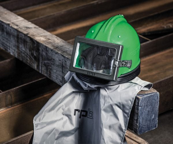 A green safety helmet with a face shield on a wooden surface, draped with a gray "rpb" logo cloth.