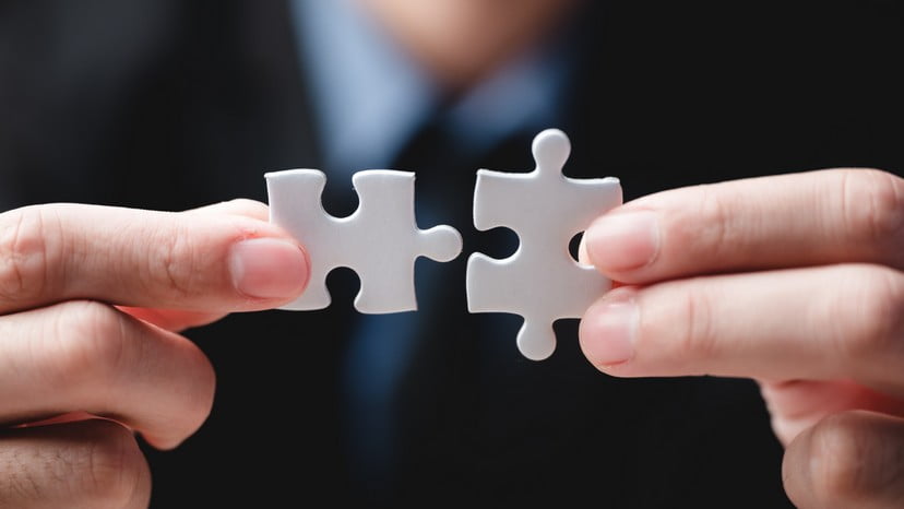 Close-up of hands fitting two white puzzle pieces together, symbolizing a perfect match or collaboration.