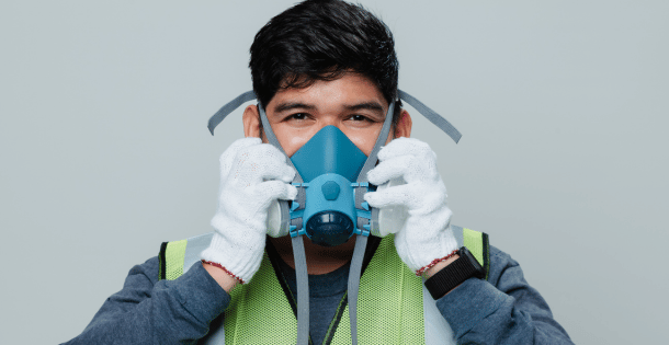A worker adjusting his respirator while wearing safety gear.