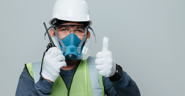 A worker wearing a respirator and safety gear giving a thumbs up.