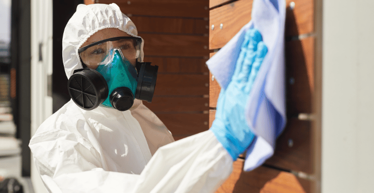 A person in protective gear wearing a respirator and cleaning a surface.
